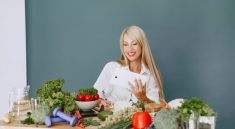 Woman using a tablet surrounded by fresh vegetables at a table, showcasing healthy lifestyle and technology.