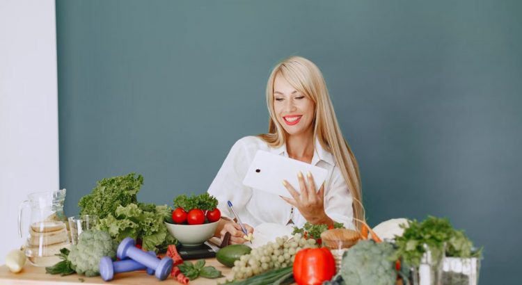 Woman using a tablet surrounded by fresh vegetables at a table, showcasing healthy lifestyle and technology.