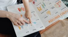A child and adult engaging with an educational book, pointing to illustrations.